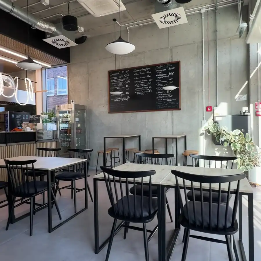 Wnętrze bistro: czarne stoliki i krzesła, lampy pod sufitem i tablica menu
